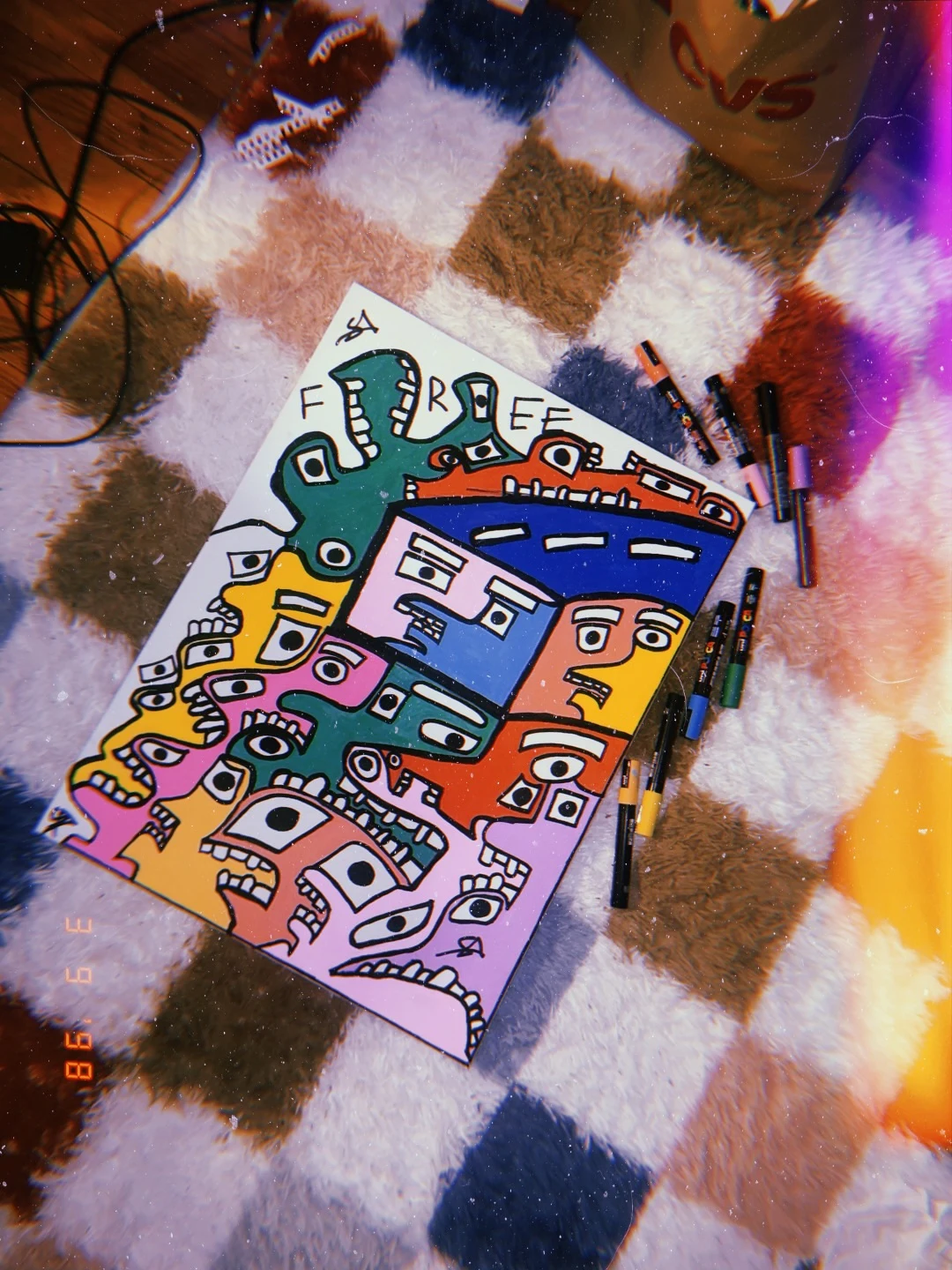 A crowd of faces in green, orange, blue, pink, yellow, and purple, each in thick black outline with square white eyes and bared teeth, pressing together beneath the word FREE hand-lettered at the top, signed SA.